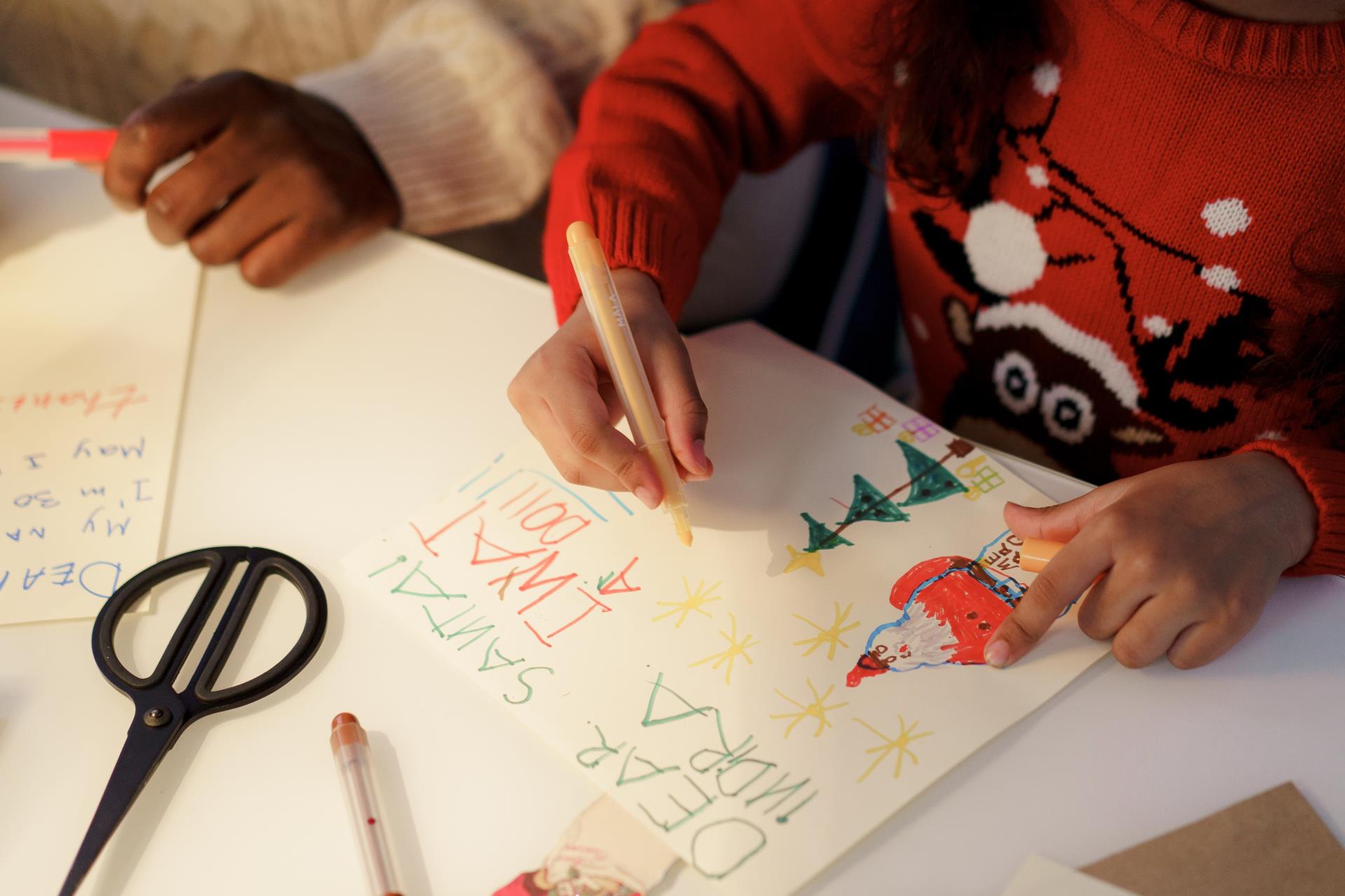 child's hands writing in home made christmas card