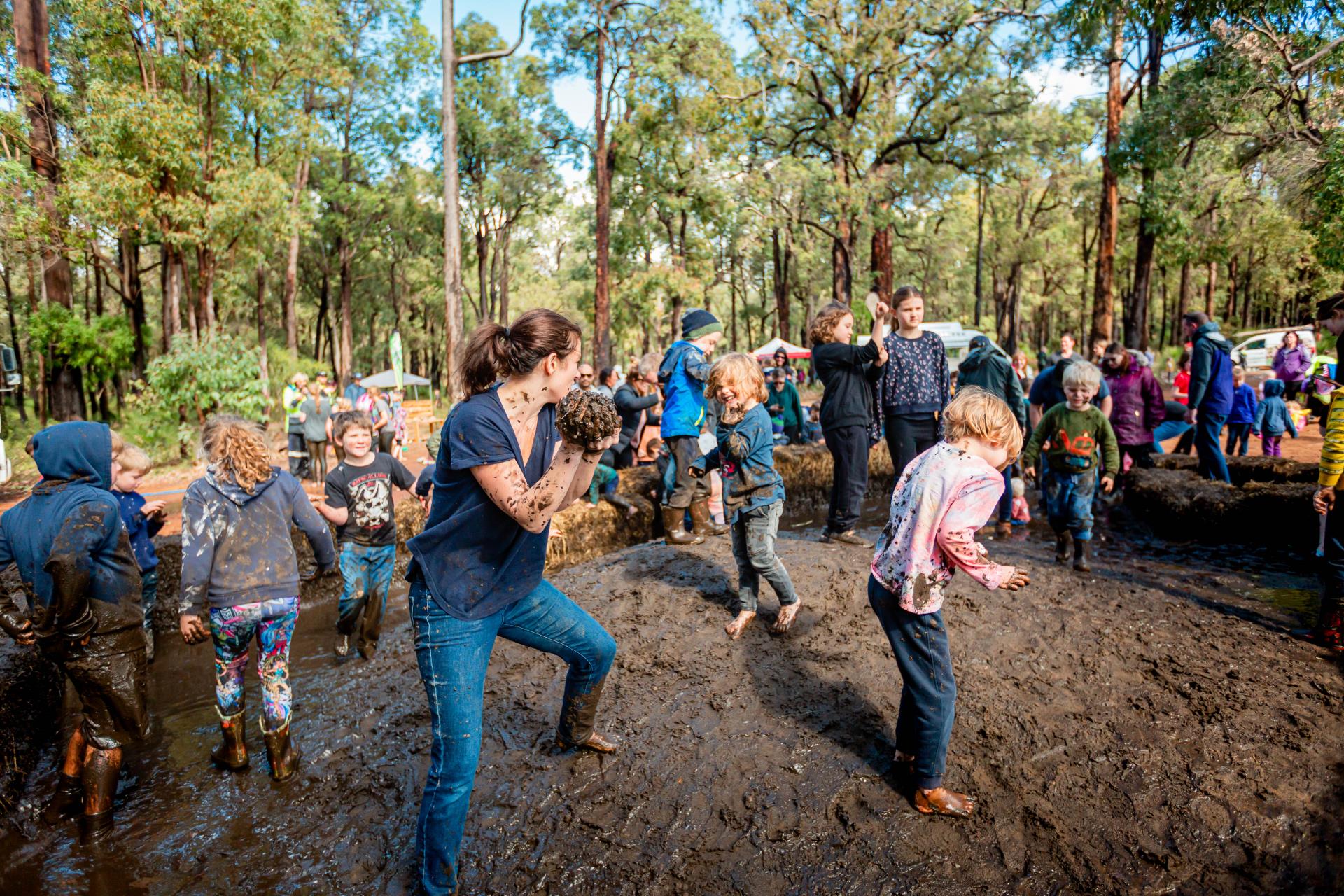 Image of people of all ages having a mud fight in a pit of mud in a bush setting