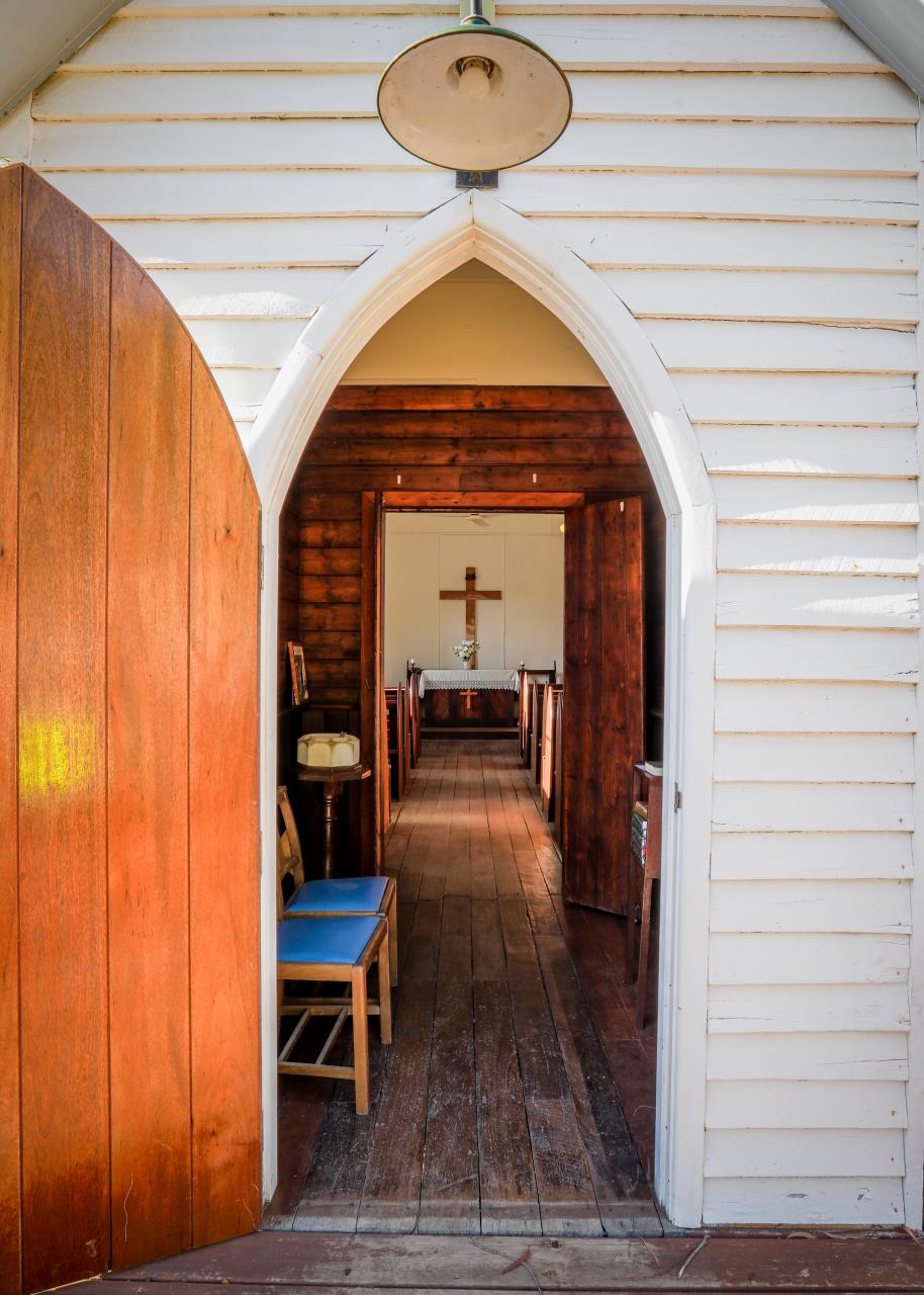 image looking inside the front door of a white wooden church, inside is brown wood walls, pews and altar 