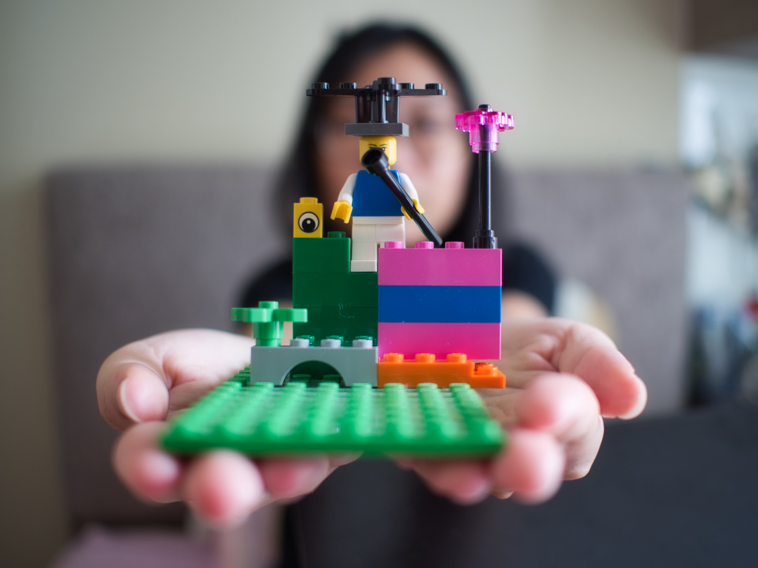 young girl in background holding out a lego board with building creation that takes up the foreground